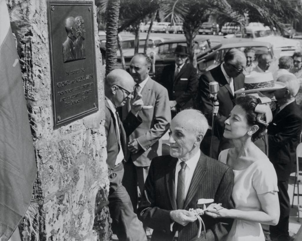 Rebyl Zain standing beside her husband George K. Zain during the dedication ceremony of the Miracle Mile plaque in Coral Gables, surrounded by civic leaders.
