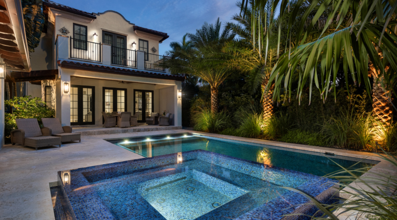 Luxury Mediterranean-style home in Coral Gables with illuminated swimming pool, spa, palm trees, and covered outdoor living space at twilight