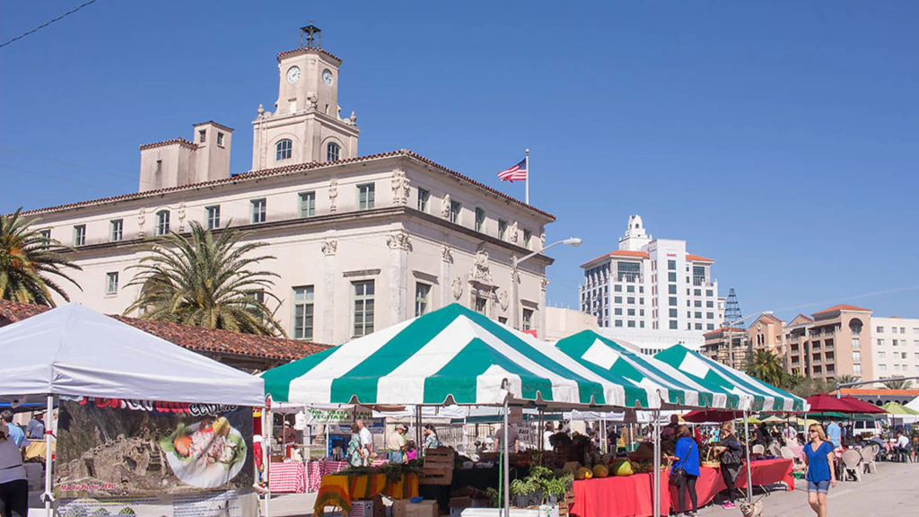 Gables Farmers Market set up in front of Coral Gables City Hall, with green-and-white tents, local vendors, and shoppers walking through on a sunny day.